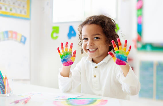 Un enfant avec de la peinture arc-en-ciel sur les mains.